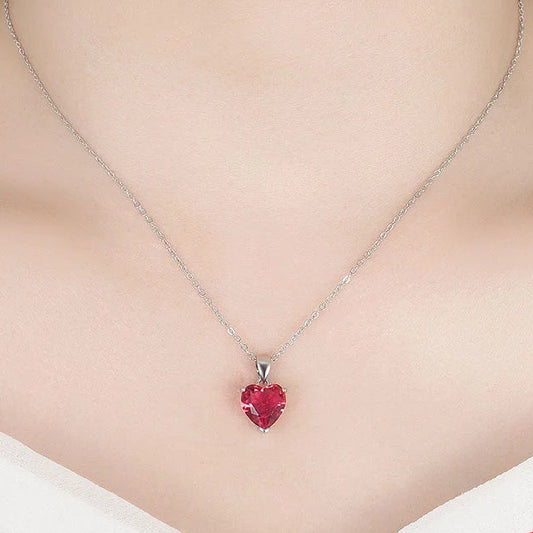 A close-up of a model's neck and chest wearing a silver necklace with a small red heart-shaped pendant