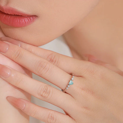 Close-up of a hand wearing a ring with a blue gemstone, against a blurred background.