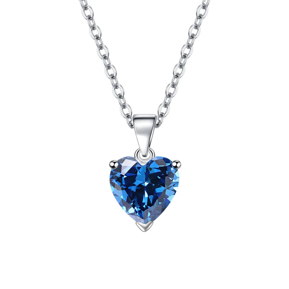 A heart-shaped blue crystal pendant necklace on a sterling silver chain, shown against a white background