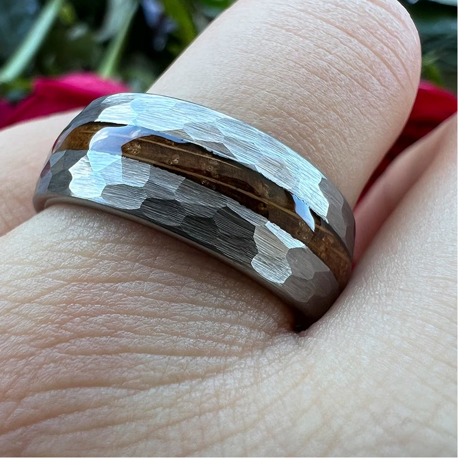 A close-up of a hammered silver band ring with a brown wood inlay, worn on a finger.