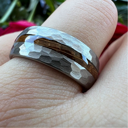 A close-up of a hammered silver band ring with a brown wood inlay, worn on a finger.