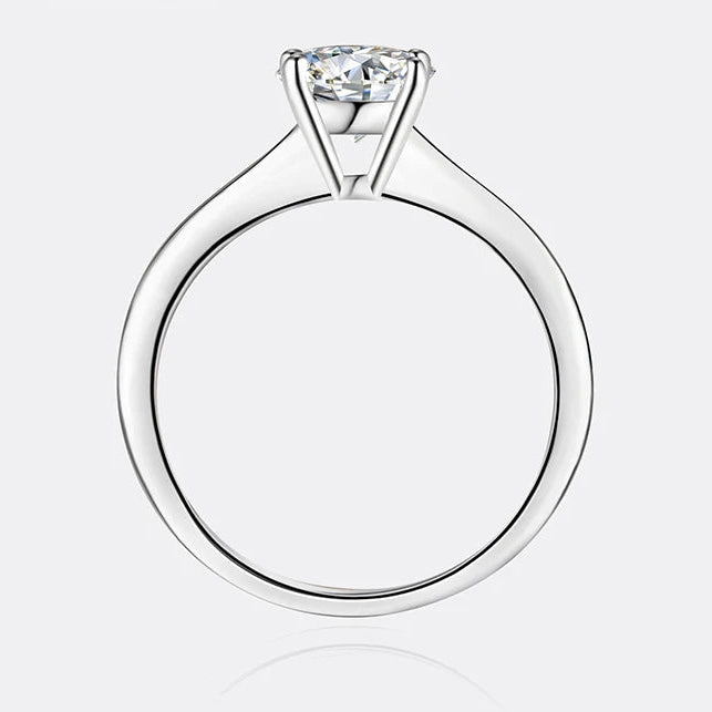A silver solitaire engagement ring with a round-cut clear gemstone, shown from a top-down view on a light gray background