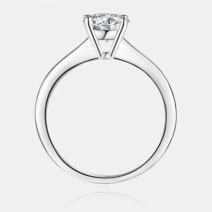 A silver solitaire engagement ring with a round-cut clear gemstone, shown from a top-down view on a light gray background