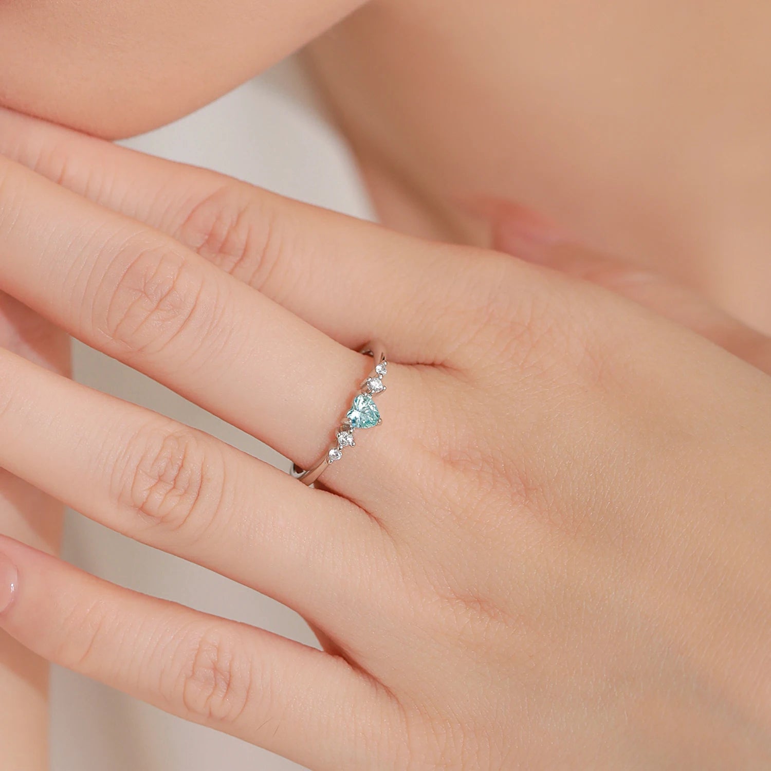 Close-up of a hand wearing a silver ring with a blue heart CZ 