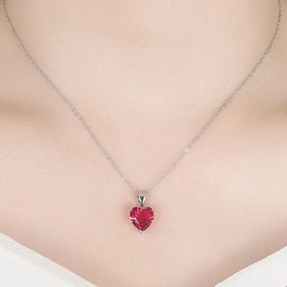 A close-up of a model's neck and chest wearing a silver necklace with a small red heart-shaped pendant