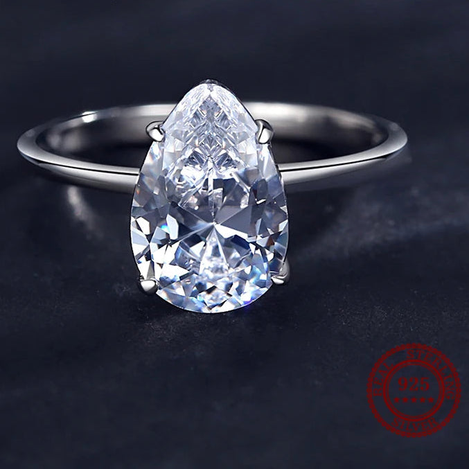 A pear-cut clear cubic zircon ring set on a polished silver band, photographed on a dark textured background