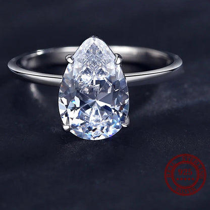 A pear-cut clear cubic zircon ring set on a polished silver band, photographed on a dark textured background