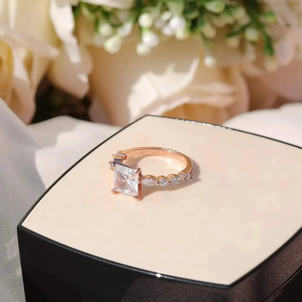 A princess-cut solitaire ring with a rose-toned band and small accent stones