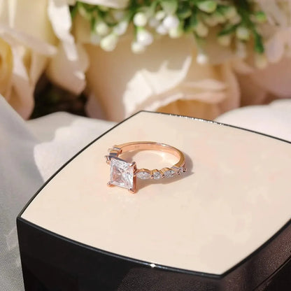 A princess-cut solitaire ring with a rose-toned band and small accent stones