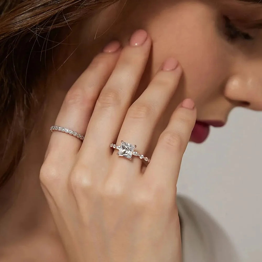 A princess-cut solitaire ring with a silver-toned band and small accent stones