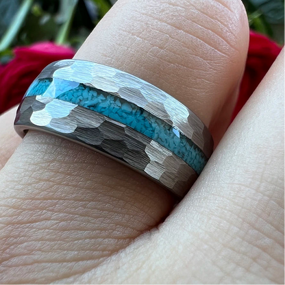 A close-up of a hammered silver ring with a vibrant turquoise blue inlay, worn on a finger. 