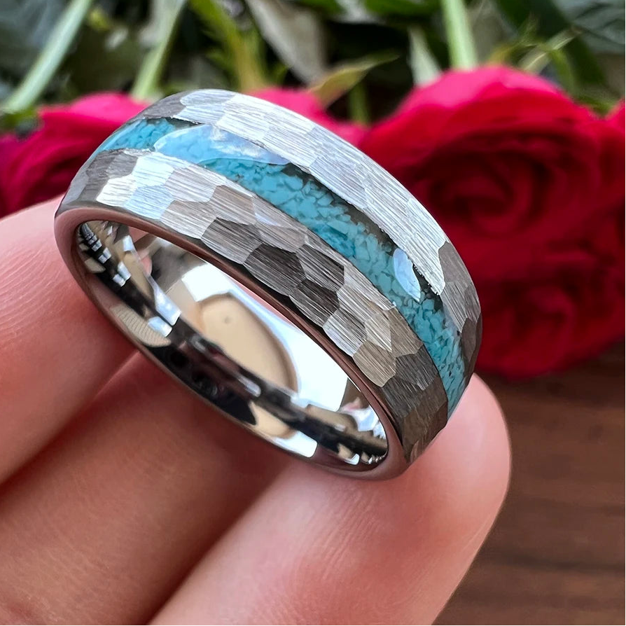 A close-up of a hammered metal ring held on a person's fingers, featuring a turquoise blue inlay